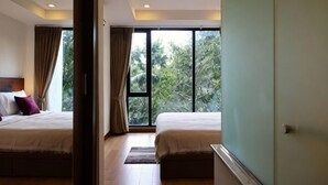 A hotel room with two beds, a large window, and a view of greenery. - Specious Luxury 2 bedrooms Apt. (Chiang Mai)