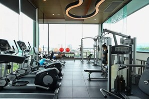 Une salle de sport équipée de machines de cardio, de matériel de musculation et offrant une vue sur la ville.