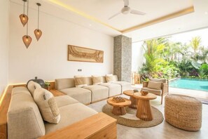 A modern living room with a sectional sofa, round wooden tables, and a view of a swimming pool. - SOL n2 villa (Bali)