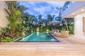 Een modern zwembadgedeelte met houten terrassen, comfortabele zitplaatsen en weelderige tropische beplanting.