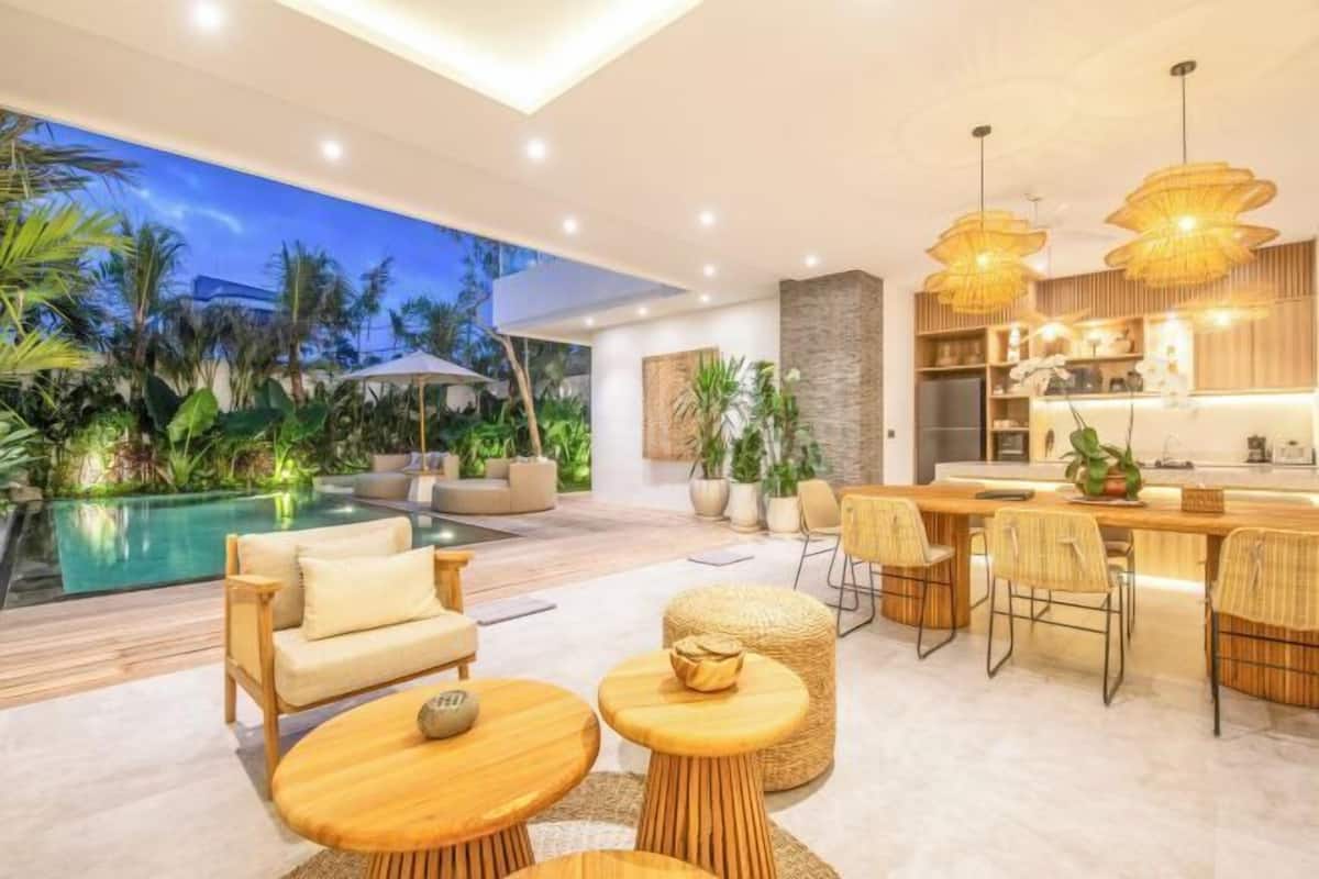 A modern outdoor living area with a pool, seating, and a kitchen area with bar seating.