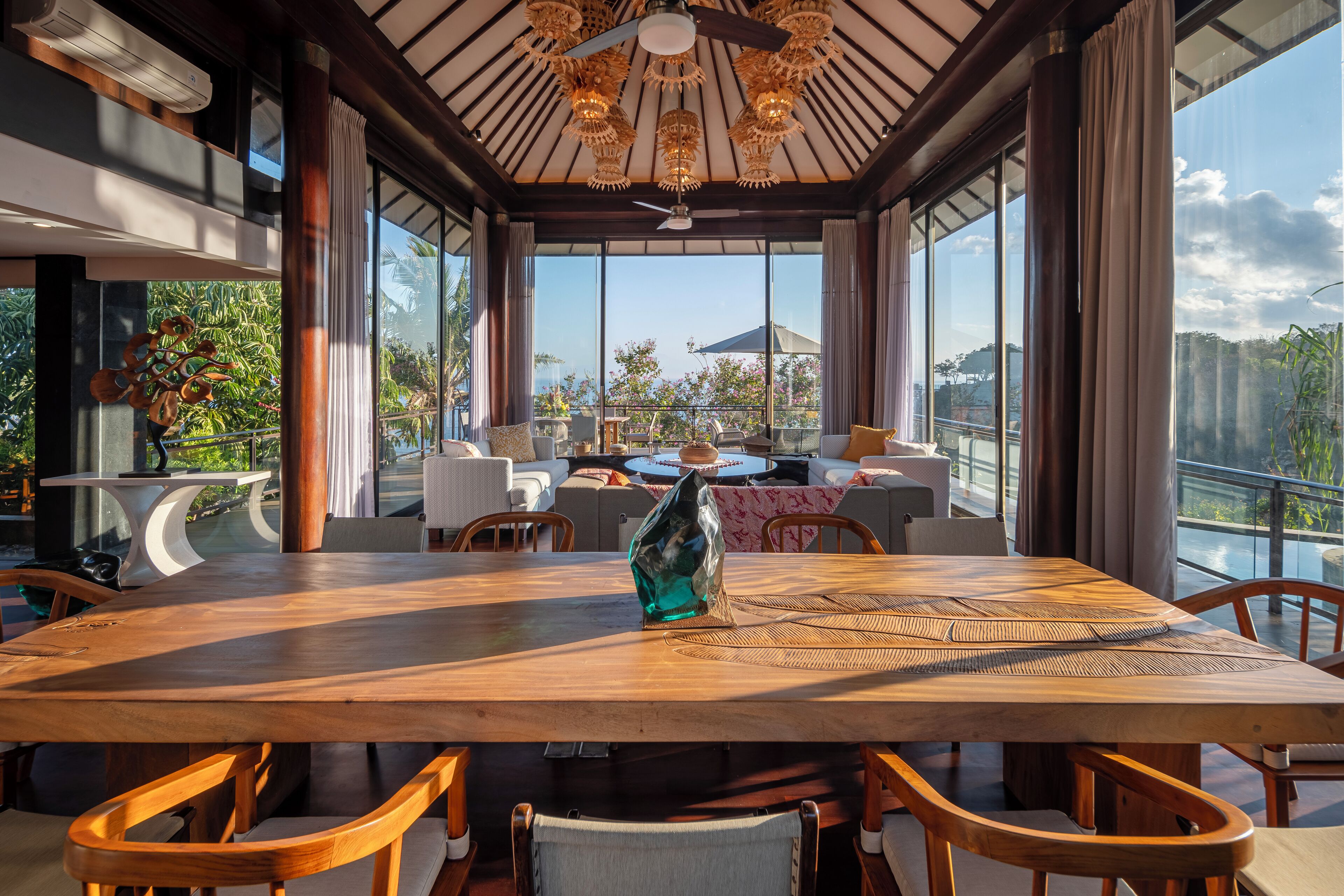 A spacious dining area with a large wooden table and chairs, a decorative glass sculpture, and a view of the outdoors through large windows.