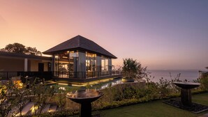 A modern building with a glass facade, a pool, and a view of the sea. - By The Cliff Bali Villa (Jimbaran)