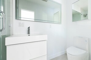 A modern bathroom with a white vanity, a toilet, and a large mirror. - Modern 2BDR Condo w/ Large Patio & Views | Avalon (San Diego)