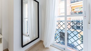Een kamer met een grote spiegel, een schuifdeur en uitzicht op een balkon met een metalen hekwerk en geparkeerde auto's.