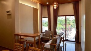 Un comedor con una mesa y sillas de madera, un sofá, y vistas al exterior a través de amplios ventanales.
