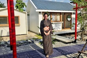 A person standing in a garden area with a house in the background. - Taka Onzen (Kaeng Khoi)