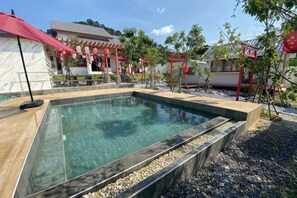 A swimming pool with a tiled deck, surrounded by a garden with small trees and a pergola. - Taka Onzen (Kaeng Khoi)