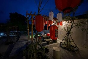 A wooden pergola with red lanterns, a stone bench, and a small table with items on it.