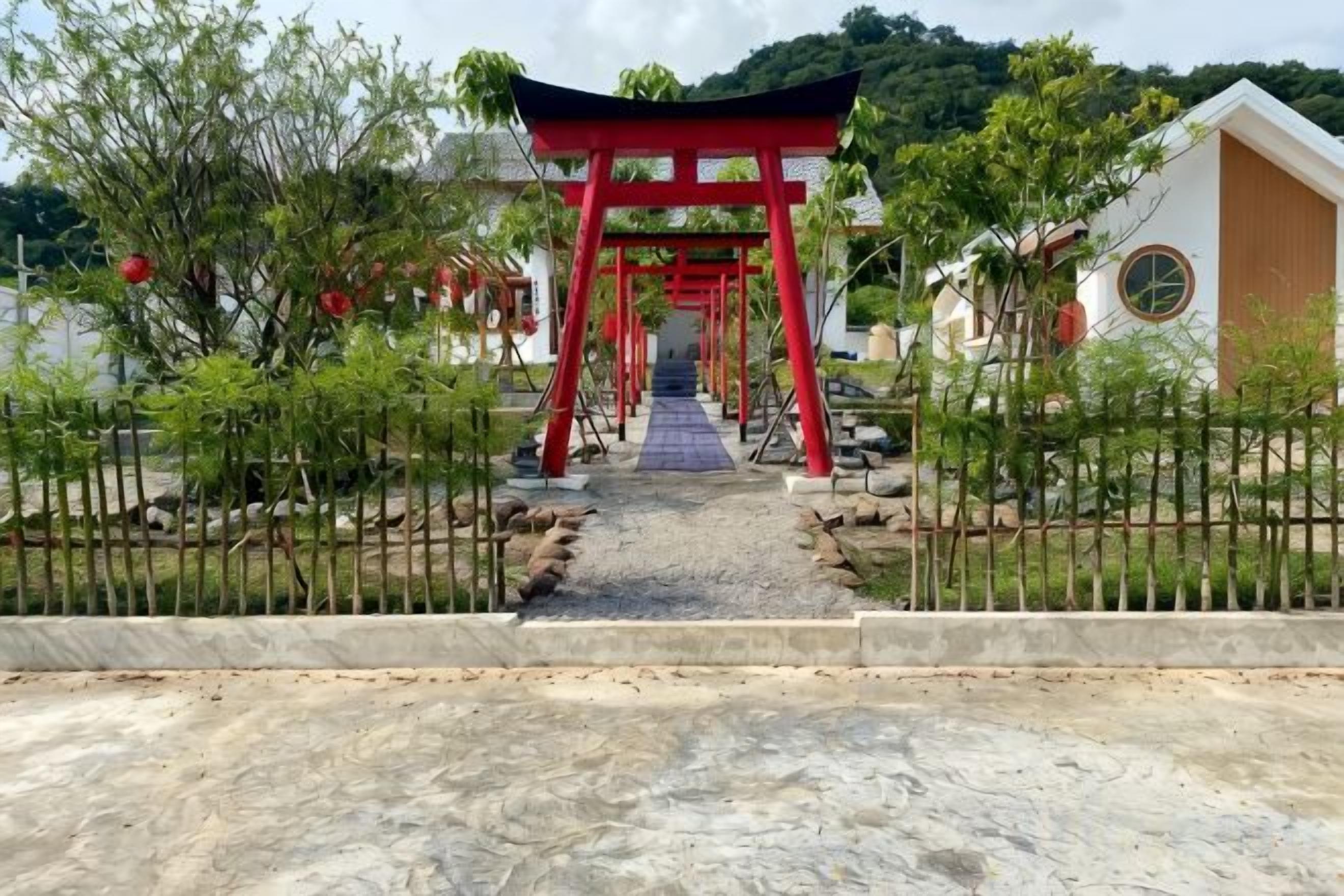 A pathway leading to a red torii gate, surrounded by greenery and a fence.