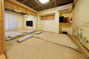 Een traditionele Japanse kamer met tatami matten, een schuifdeur, een bevestigde televisie en een muurschildering.