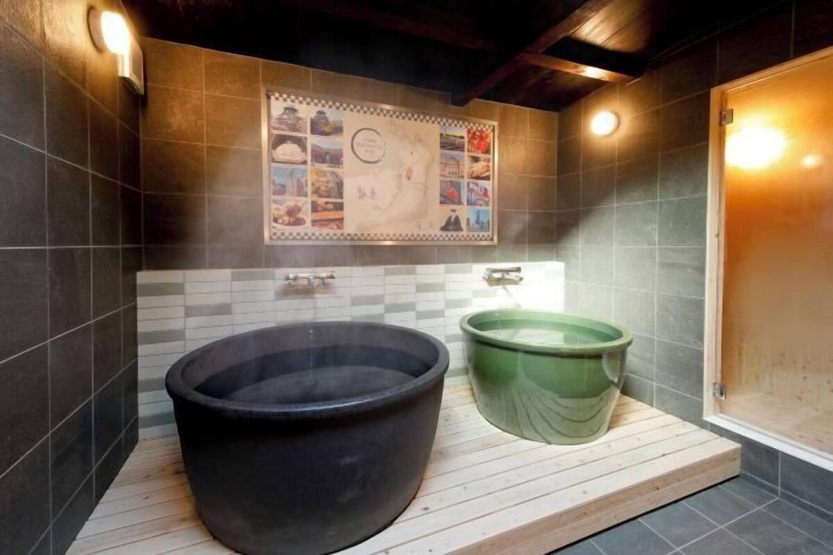 Un baño moderno con una bañera negra grande, una bañera de inmersión verde y una zona de ducha con azulejos.