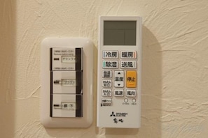 Ein an der Wand montiertes Thermostat und Bedienfeld mit japanischen Schriftzeichen, vermutlich zur Steuerung der Raumtemperatur und des Ventilators.