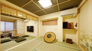 Una habitación japonesa tradicional con suelo de tatami, una mesa baja de tatami, un sofá de tatami, un biombio shoji, un ventilador de techo y un televisor montado.