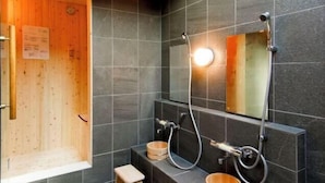 Un baño moderno con azulejos oscuros, una puerta de madera y un espejo grande.