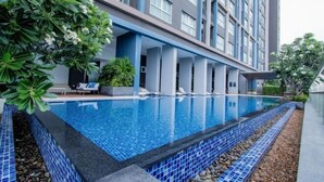 A modern hotel with a swimming pool, lounge chairs, and a well-maintained garden.