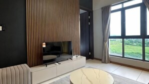 A modern living room with a large window, a flat-screen TV, and a sofa. - Urban Retreat @ K Avenue • Pool • Paid Parking (Donggongon)