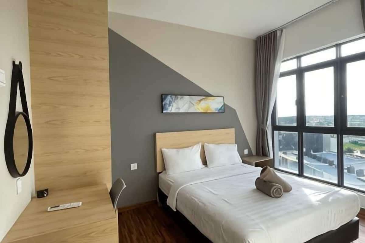 A hotel room with a bed, a window with a city view, a painting on the wall, and a wooden accent wall.