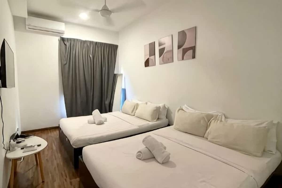 A hotel room with two beds, a small table, a TV, and a window with curtains.