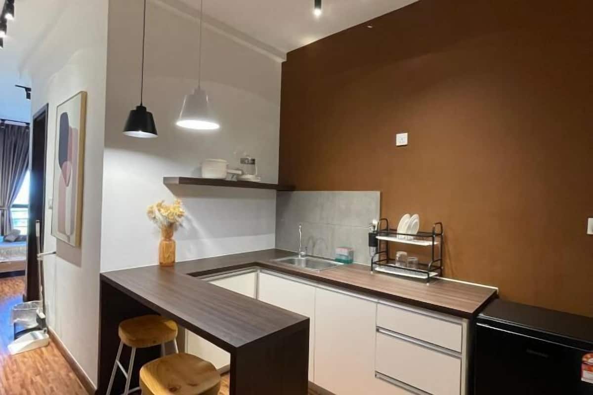 A modern kitchen with a central island, bar stools, pendant lighting, and a built-in dishwasher.