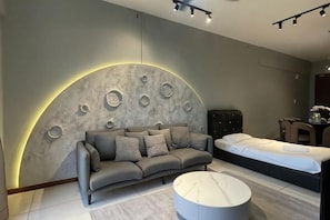 A modern room with a sofa, a bed, a round coffee table, and a wall with circular patterns. - Urban Retreat @ K Avenue • Pool • Paid Parking (Donggongon)