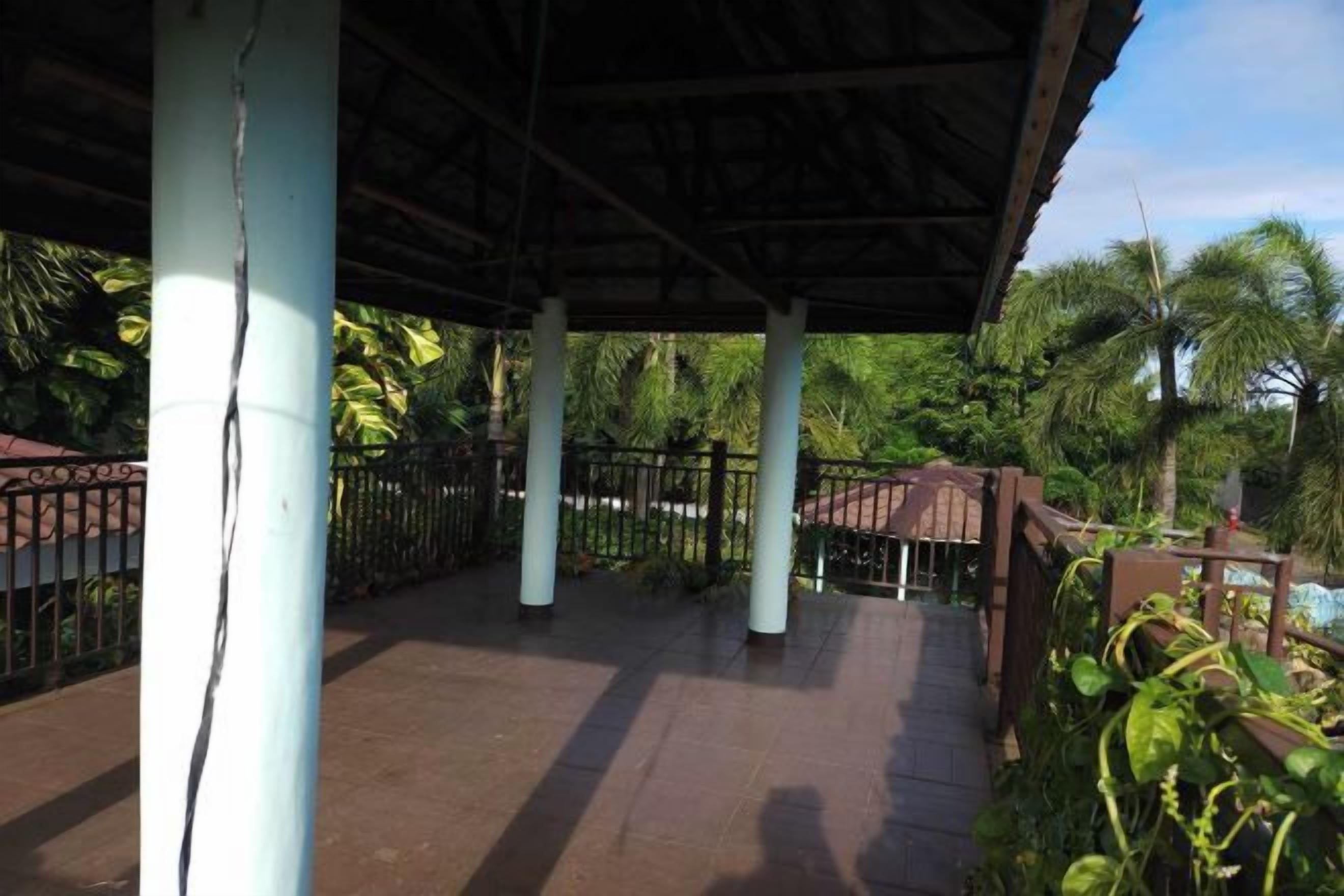A covered outdoor area with columns, a fence, and greenery.