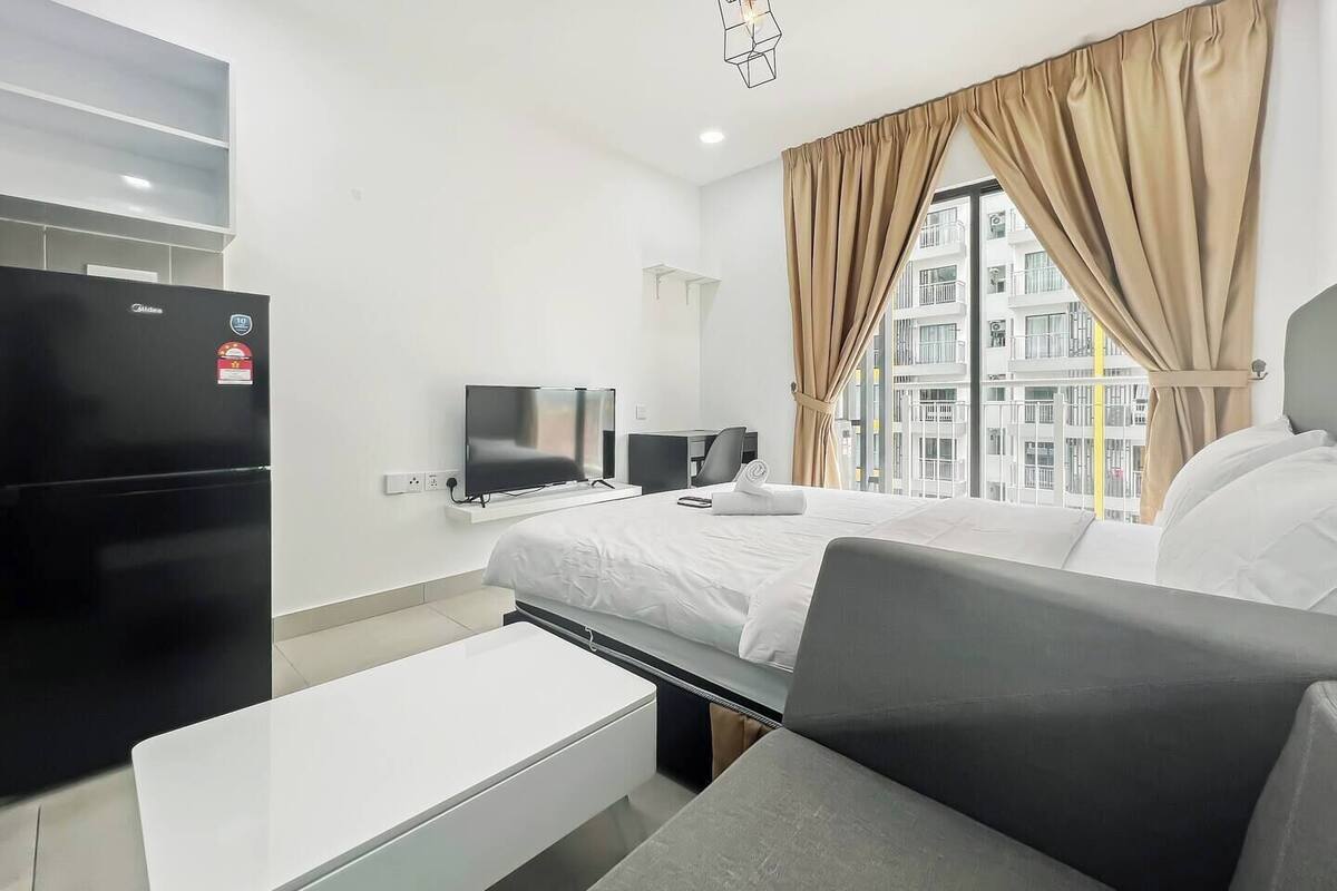 Une chambre d’hôtel moderne équipée d’un lit, d’une télévision, d’un réfrigérateur et d’une fenêtre avec des rideaux.