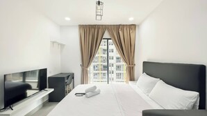 Een moderne hotelkamer met een groot bed, een televisie, een bureau en uitzicht op de stad door grote ramen.