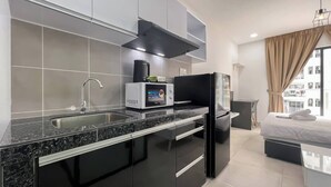 Een moderne keuken met een granieten aanrechtblad, een roestvrijstalen spoelbak en zwarte kasten. Er is een magnetron, een zwarte afzuigkap en een koelkast. De kamer heeft een groot raam met beige gordijnen en een bed met witte lakens.