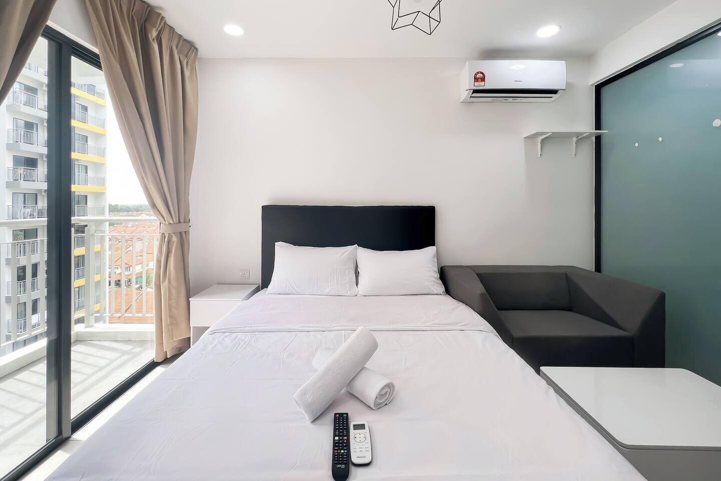 A hotel room with a large bed, a bedside table, a remote control, and an air conditioning unit.