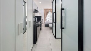 Een moderne, smalle gang met een keuken aan de linkerkant, een bed met raam in het midden en een glazen deur aan de rechterkant.