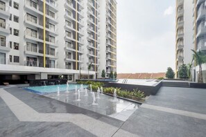 A modern residential building with multiple balconies, a central courtyard with a pool and water features, and a flat-roofed structure in the background. - DK Impian Luxury Condominiums Smarthome (Shah Alam)