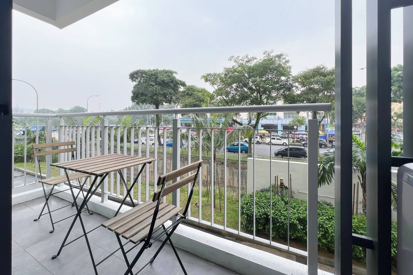 Ein Balkon mit Tisch und zwei Stühlen, Blick auf eine Straße mit Autos und Grünflächen.