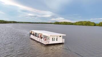 A stationary houseboat with a deck and windows, floating on a calm body of water.