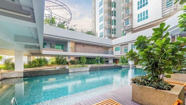 Un espace piscine intérieur moderne, doté d’une terrasse en bois, de chaises longues et d’un jardinier avec des plantes vertes.
