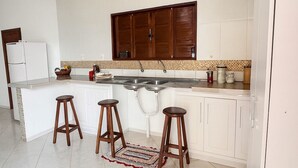 A kitchen with white cabinets, a double sink, and wooden stools. - Amazon House with Pool, Pool Table, BBQ, 5 min from the Beach (Macapá)