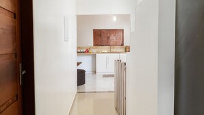 A hallway leading to a kitchen with white walls, a wooden door, and a tiled floor. - Amazon House with Pool, Pool Table, BBQ, 5 min from the Beach (Macapá)