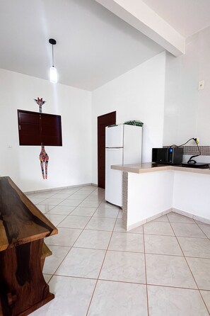 A modern kitchen with a white refrigerator, a microwave, and a wooden dining table. - Amazon House with Pool, Pool Table, BBQ, 5 min from the Beach (Macapá)