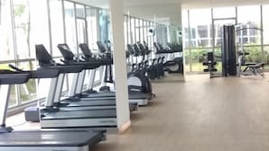 A gym with treadmills lined up against large windows, a weight machine, and a bench. - Gold Coast Pik Atlantic Sea View Apartment Minimum 2 Nights Stay (North Jakarta)