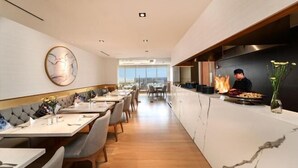 A modern restaurant interior with a long counter, seating area, and a chef preparing food. - Gold Coast Pik Atlantic Sea View Apartment Minimum 2 Nights Stay (North Jakarta)