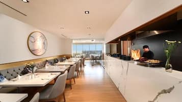 A modern restaurant interior with a long counter, seating area, and a chef preparing food.