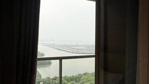 A view from a window with curtains, overlooking a river and a bridge. - Gold Coast Pik Atlantic Sea View Apartment Minimum 2 Nights Stay (North Jakarta)
