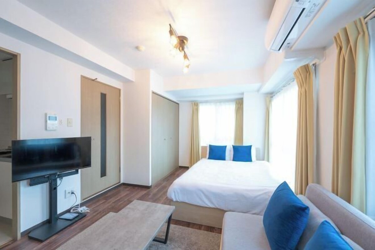A hotel room with a bed, a TV, a desk, and a window with curtains.