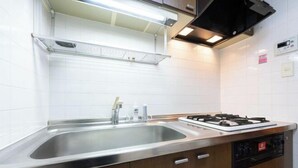 A kitchen with a stainless steel sink, a gas stove, wooden cabinets, and a white tiled backsplash. - Raiwa Mansion Minami Azabu (Tokyo)