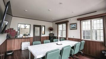 A conference room with a long table, chairs, a television, and a window with blinds.