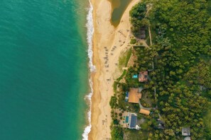 An aerial view of a beachside property with a swimming pool, a small building, and dense greenery.