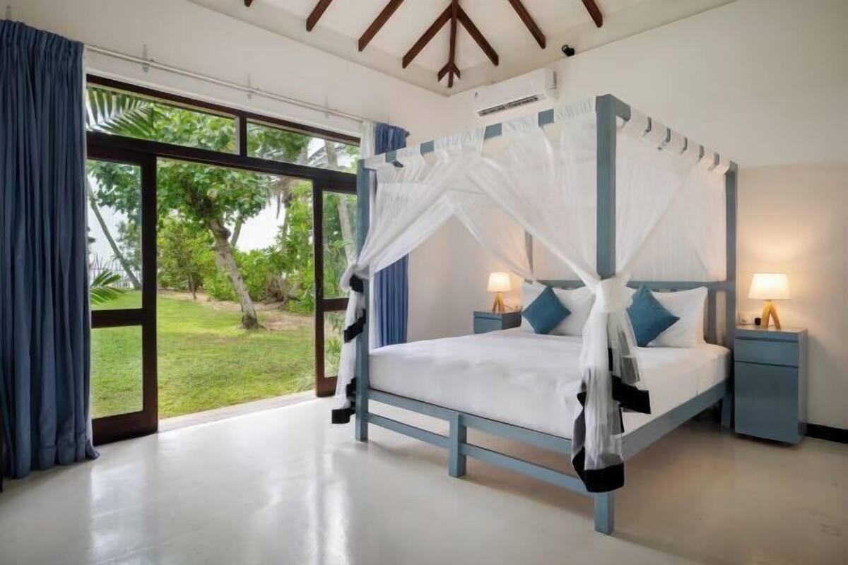 Un dormitorio con cama con dosel, dos mesitas de noche y un ventanal con cortinas.