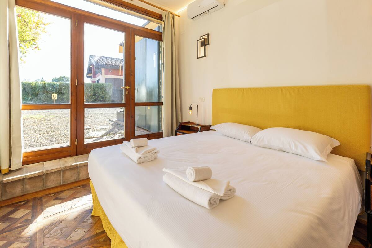 A hotel room with a large bed, a wooden headboard, and a view through a glass door.