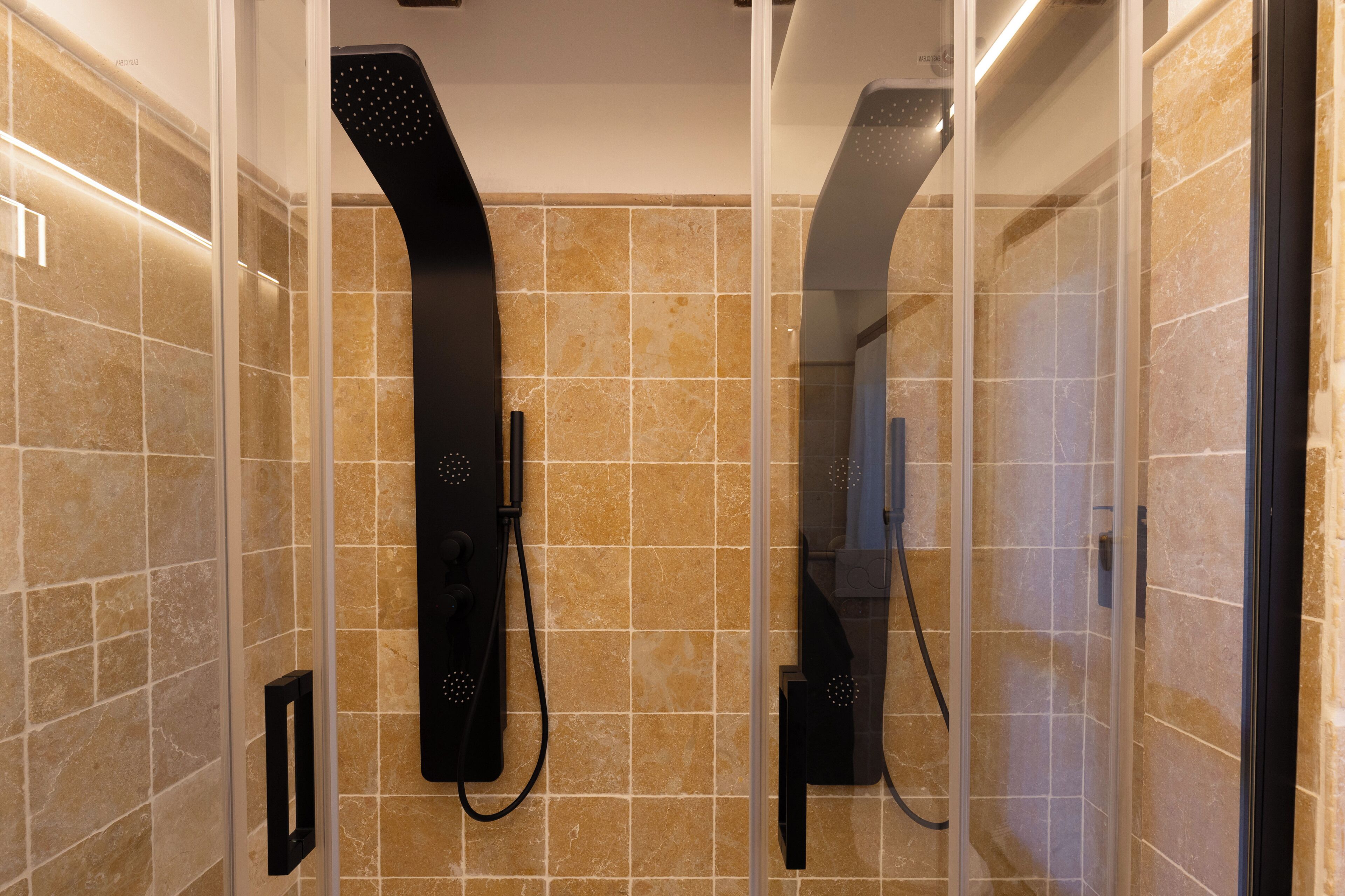 A modern bathroom with a glass-enclosed shower, beige tiles, and a black handheld showerhead.