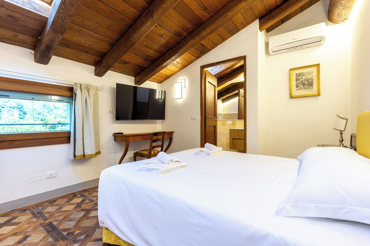 A hotel room with a bed, a TV, a desk, and a window with curtains.